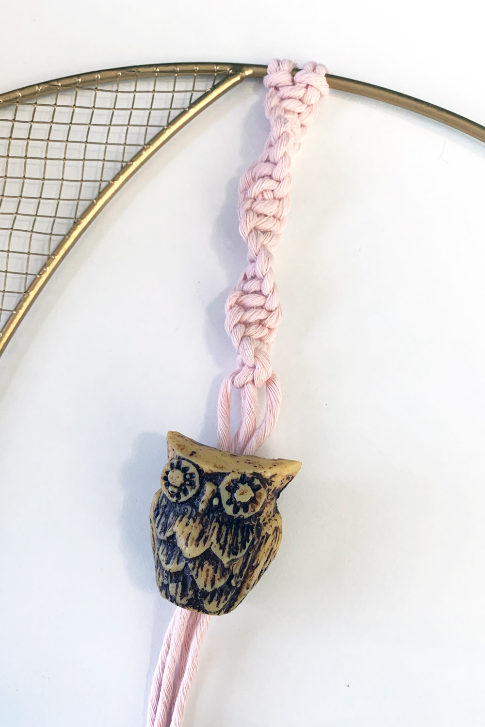 A large wooden owl bead slid onto the unfinished end of a pink macrame cord twist.