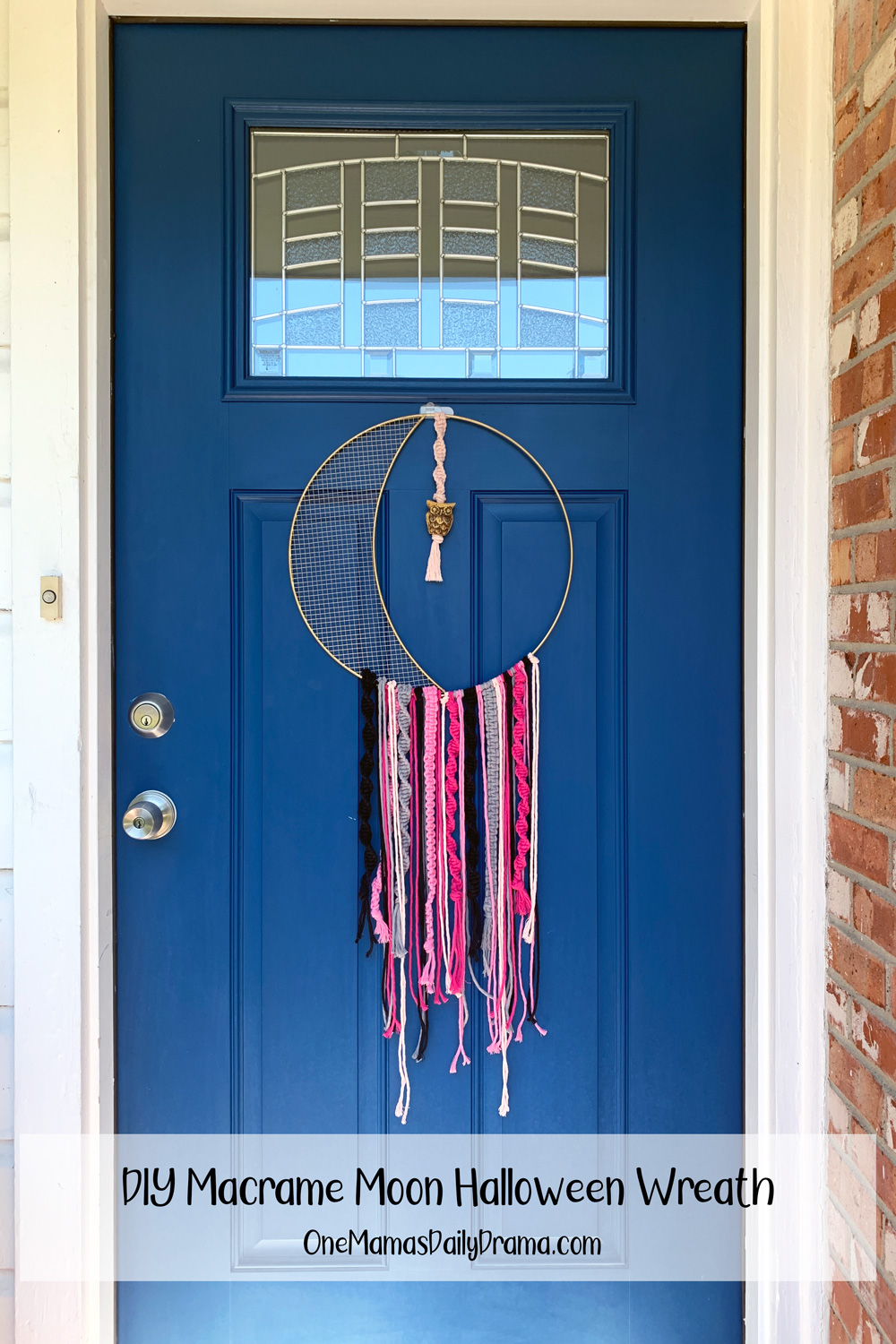 A crescent moon metal wreath frame with macrame knots and cords in pink and black hanging on a front door.