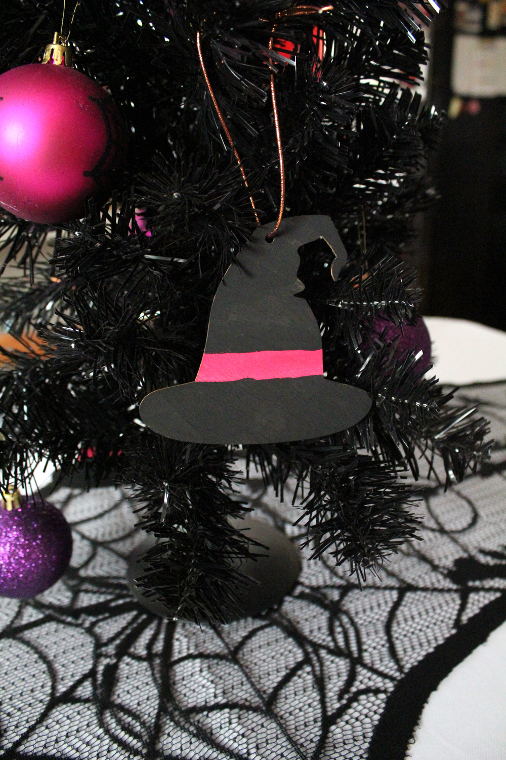 Wooden witch hat ornament painted black with a pink band.