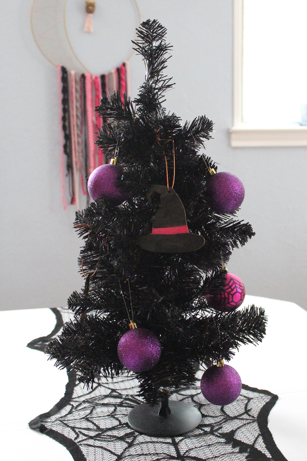 Black artificial tree decorated with pink and purple ball ornaments and black wooden witch hats.