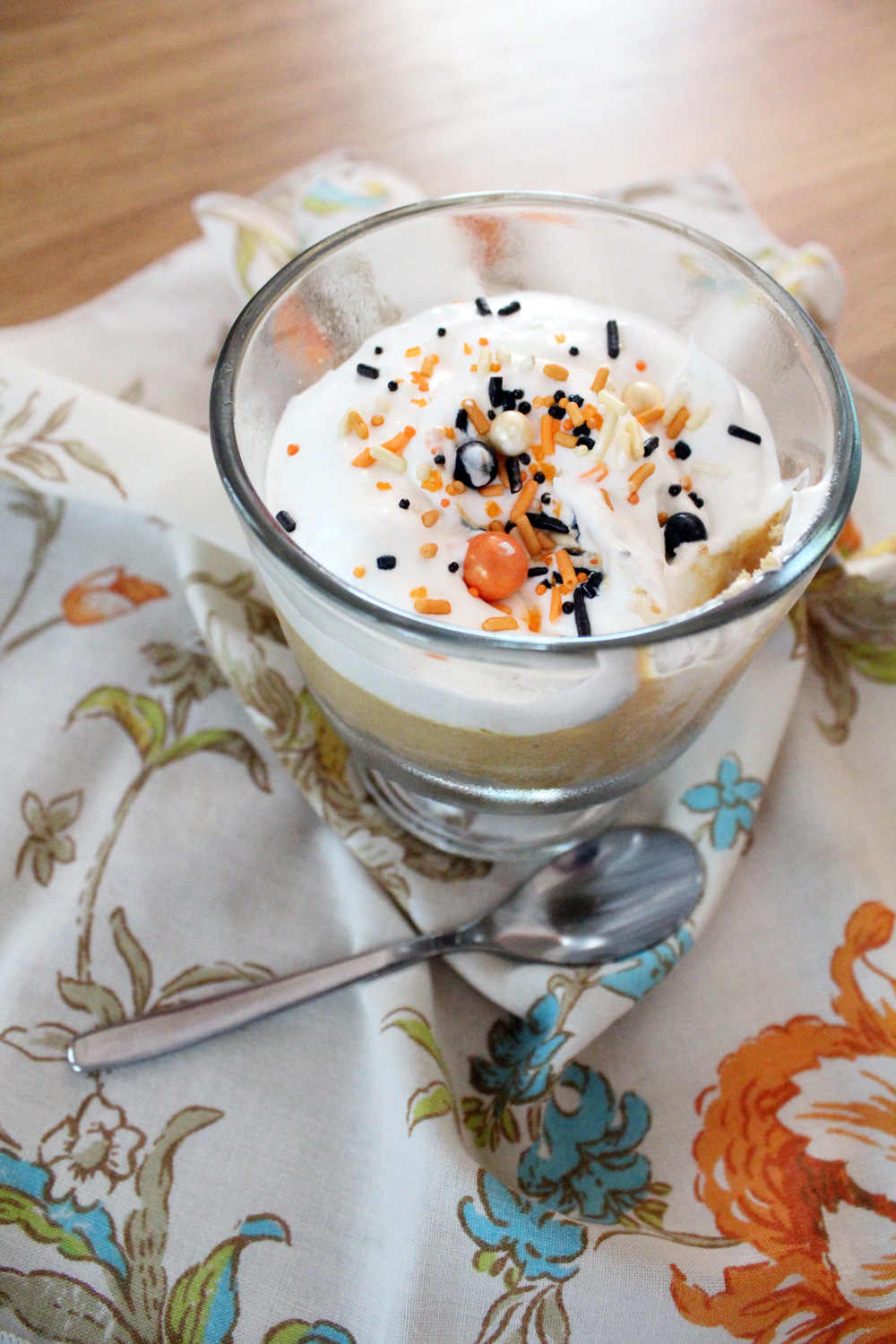 Glass with pumpkin pudding and a graham cracker crust, topped with whipped cream and fall sprinkles.