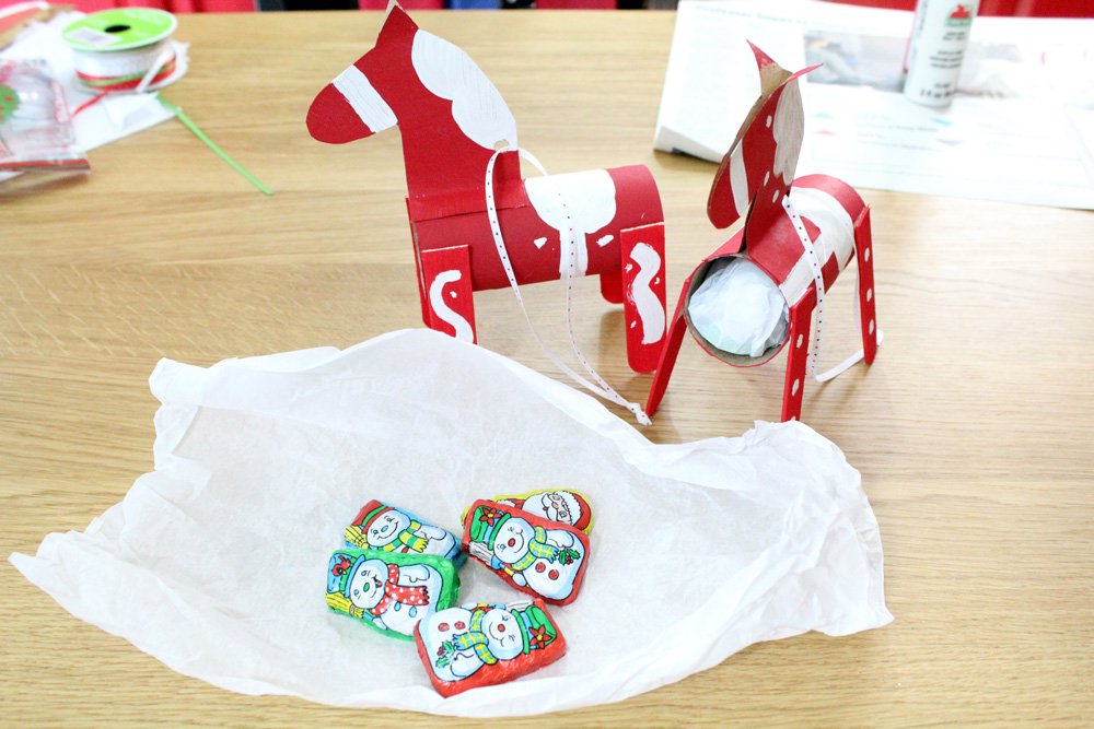 Tissue paper with 5 pieces of wrapped chocolate snowmen beside a paper tube horse.