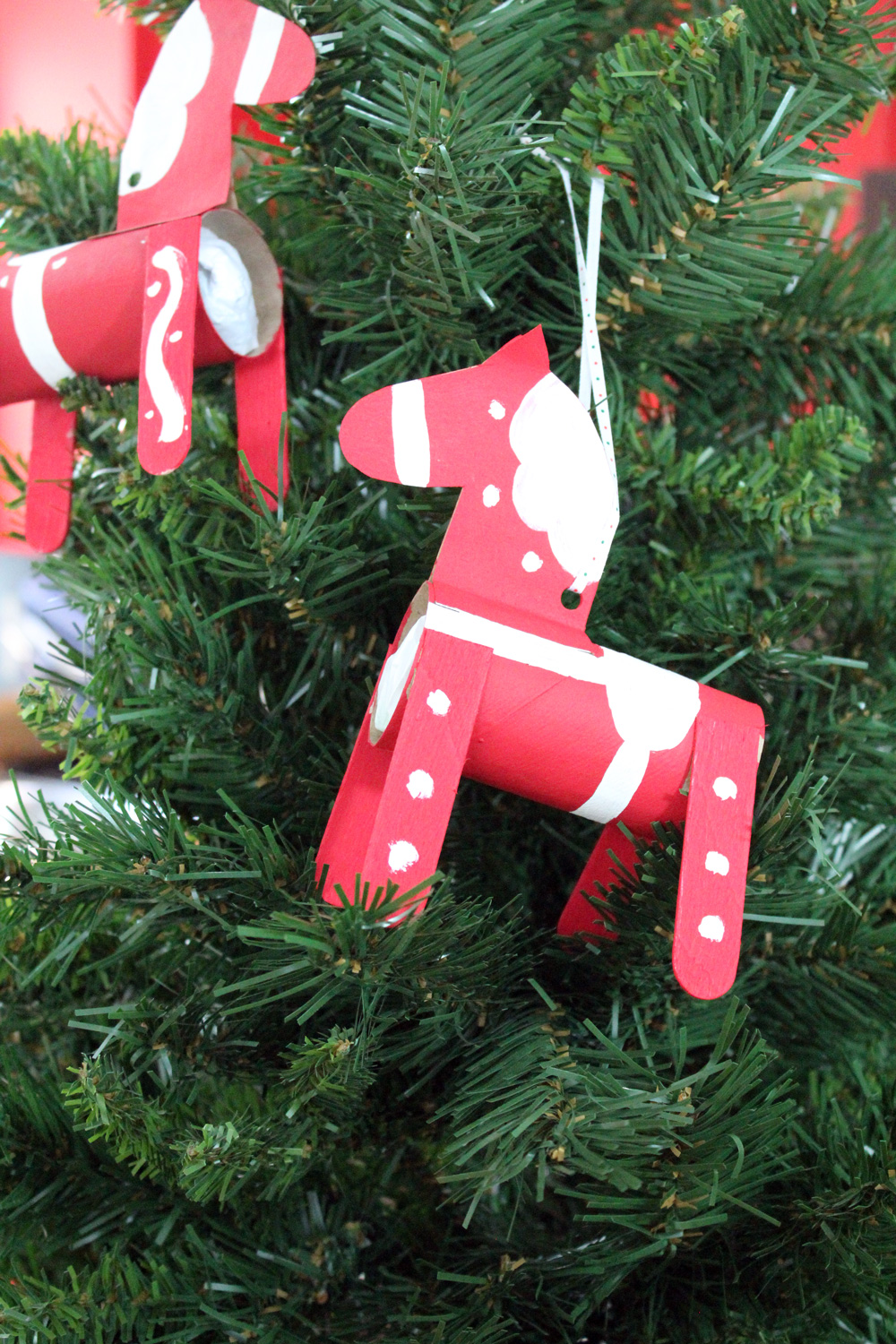 2 handmade dala horse Christmas ornaments hanging on a green tree.