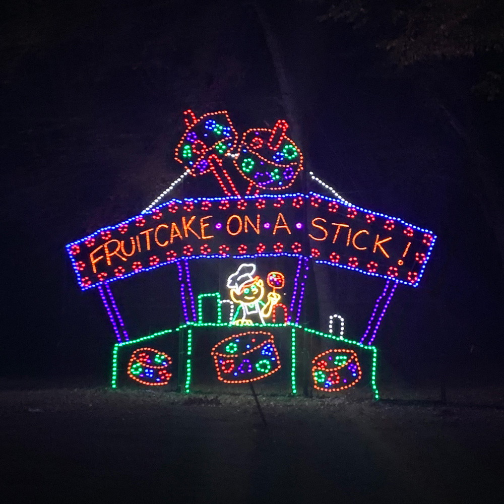 Christmas light display of an elf vendor at a fruitcake-on-a-stick stand.