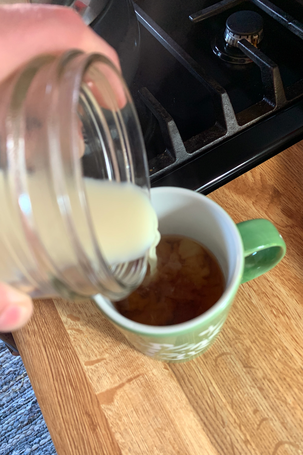 Pouring hot soy milk from a glass into a cup of tea.