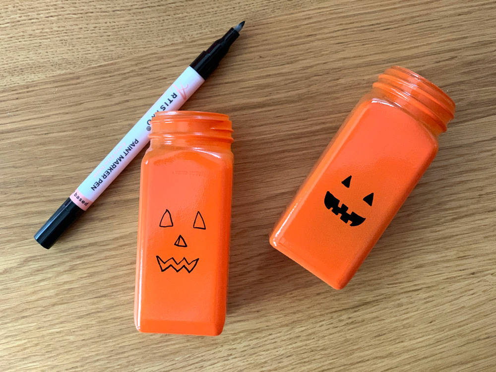 2 small spice jars painted orange with black paint pen faces.