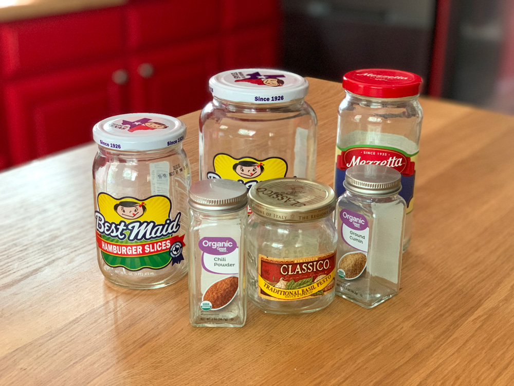 Several empty glass containers of varying sizes labeled for pickles, olives, and spices.