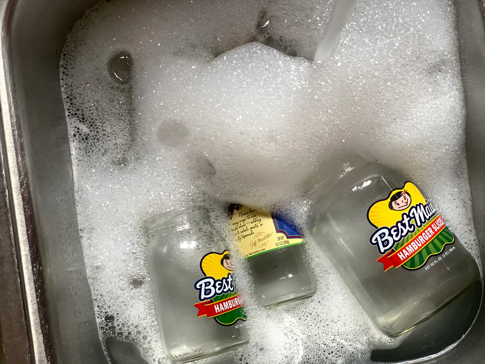 A sink full of soapy water and empty pickle jars.