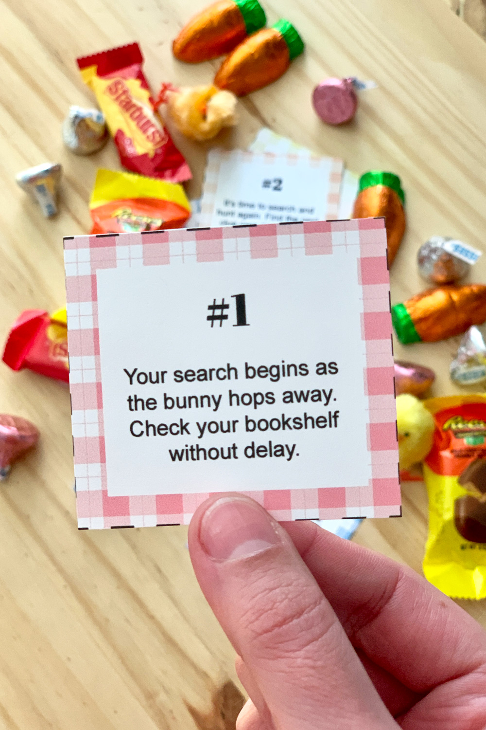 Hand holding a scavenger hunt clue that reads "#1: Your search begins as the bunny hops away. Check your bookshelf without delay."