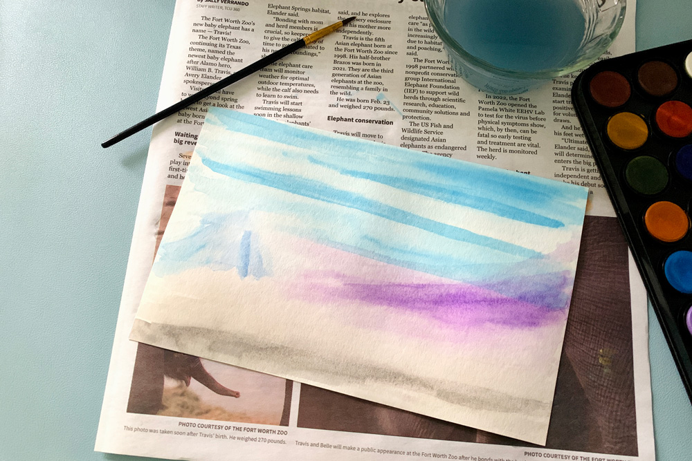 Painting a watercolor landscape background in blue, purple, and gray.