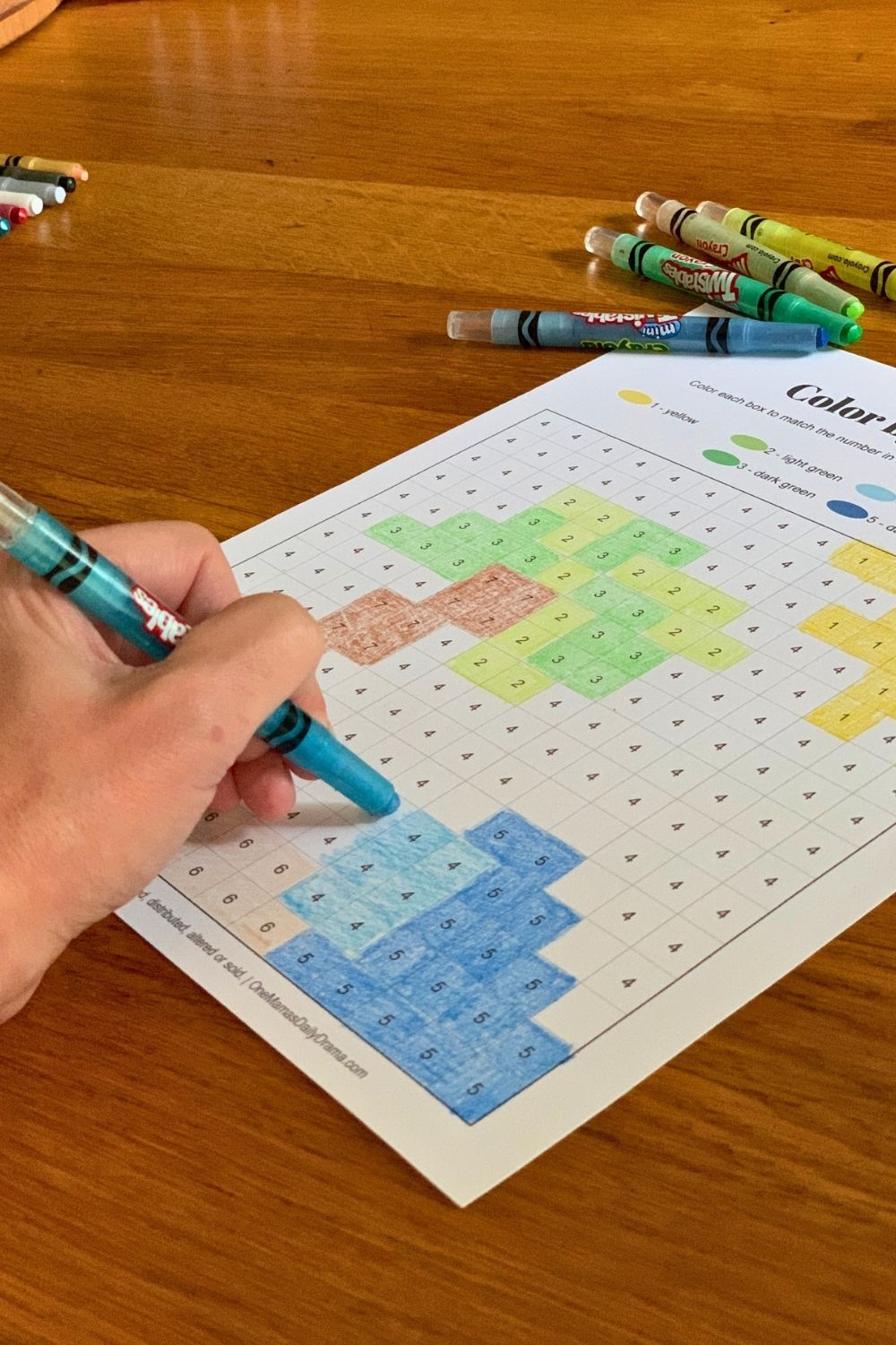 Using a blue crayon to color the boxes on a coloring page.