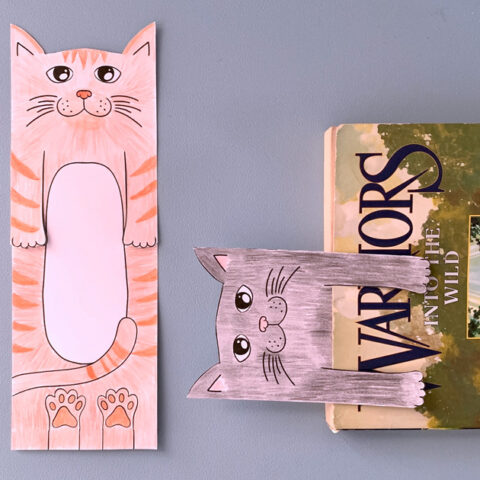 An orange striped cat bookmark beside a black cat bookmark stuck inside a book.