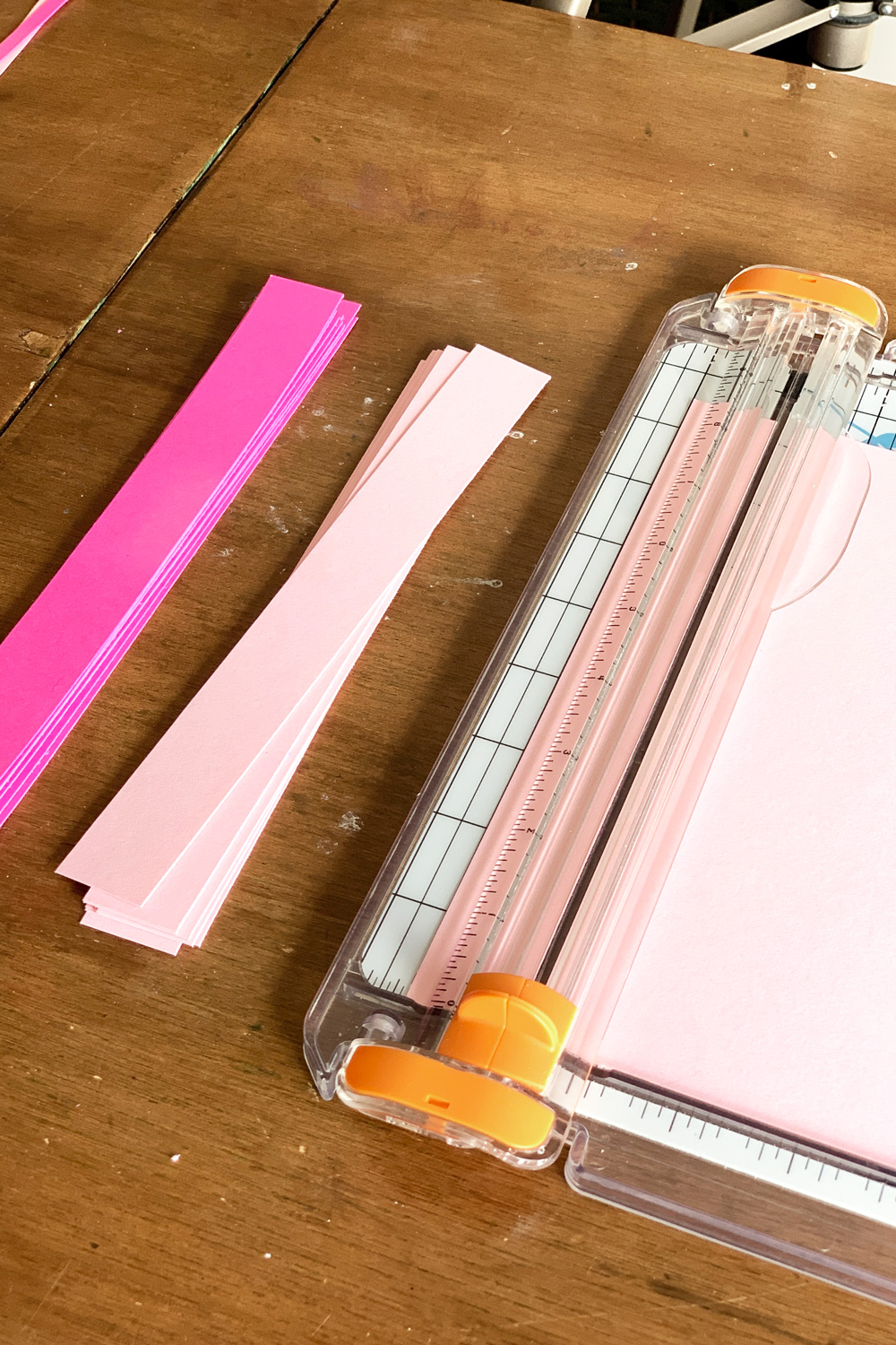 Using a paper trimmer to cut pink card stock into 1-inch wide strips.