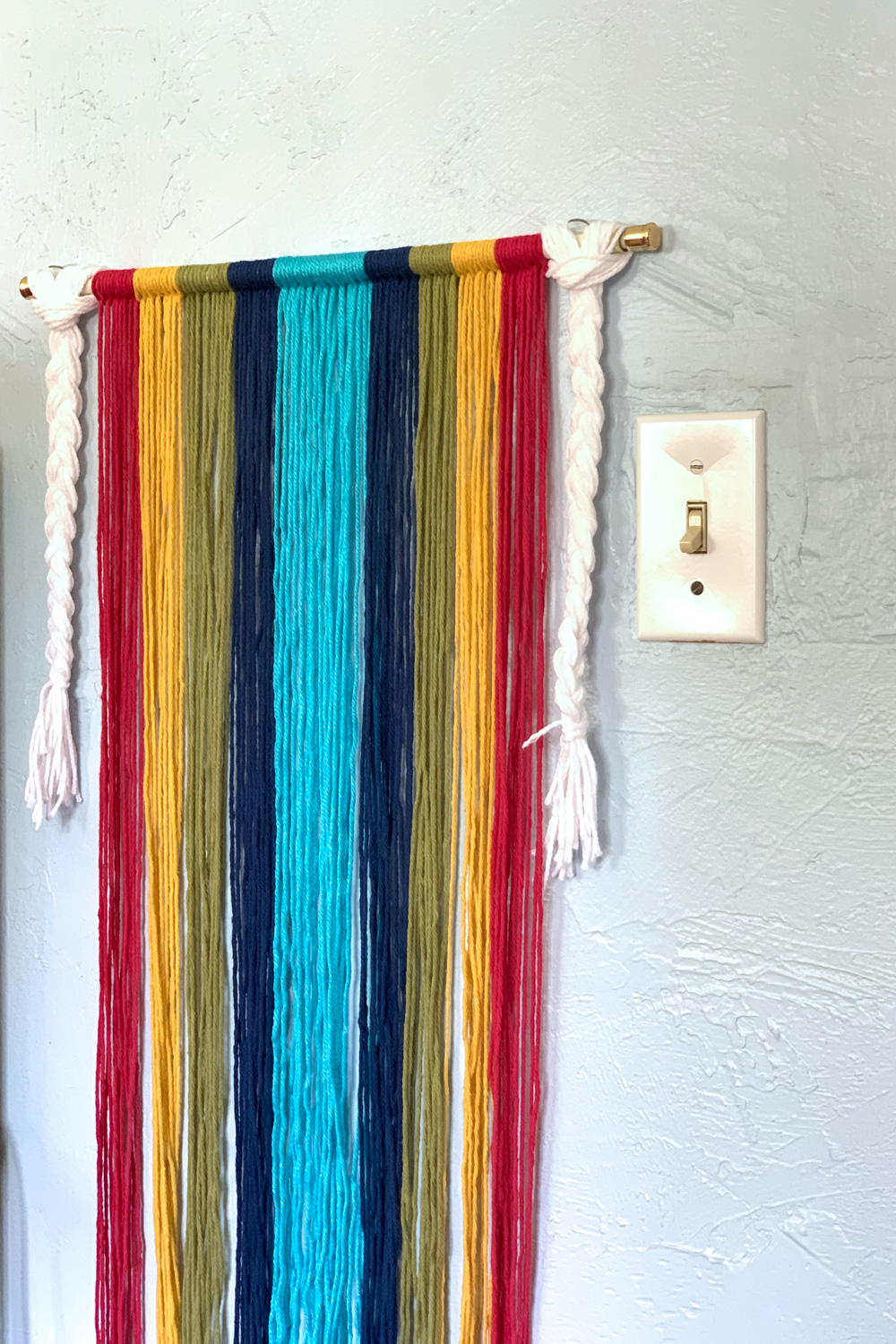 Rainbow yarn wall hanging in red, yellow, green, and two shades of blue.