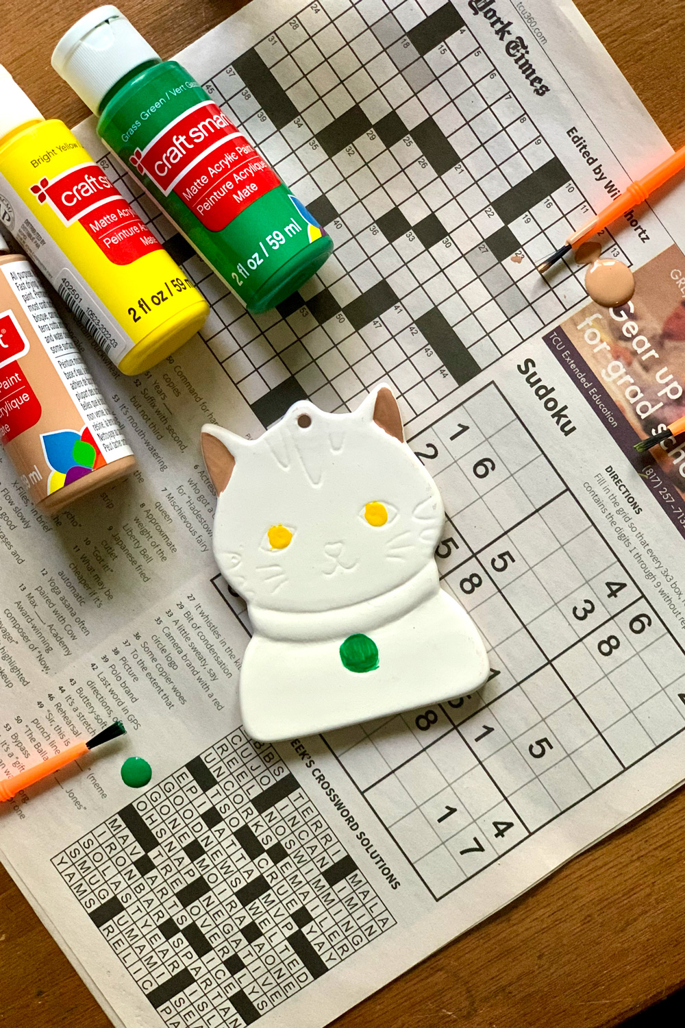 A cat ornament with the eyes painted yellow, collar tag painted green, and inside ears brown.