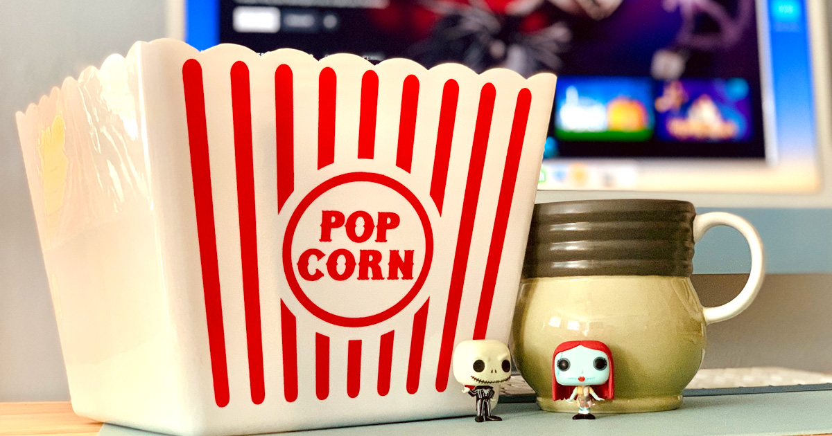 A popcorn box and mug of cocoa in front of a tv screen.