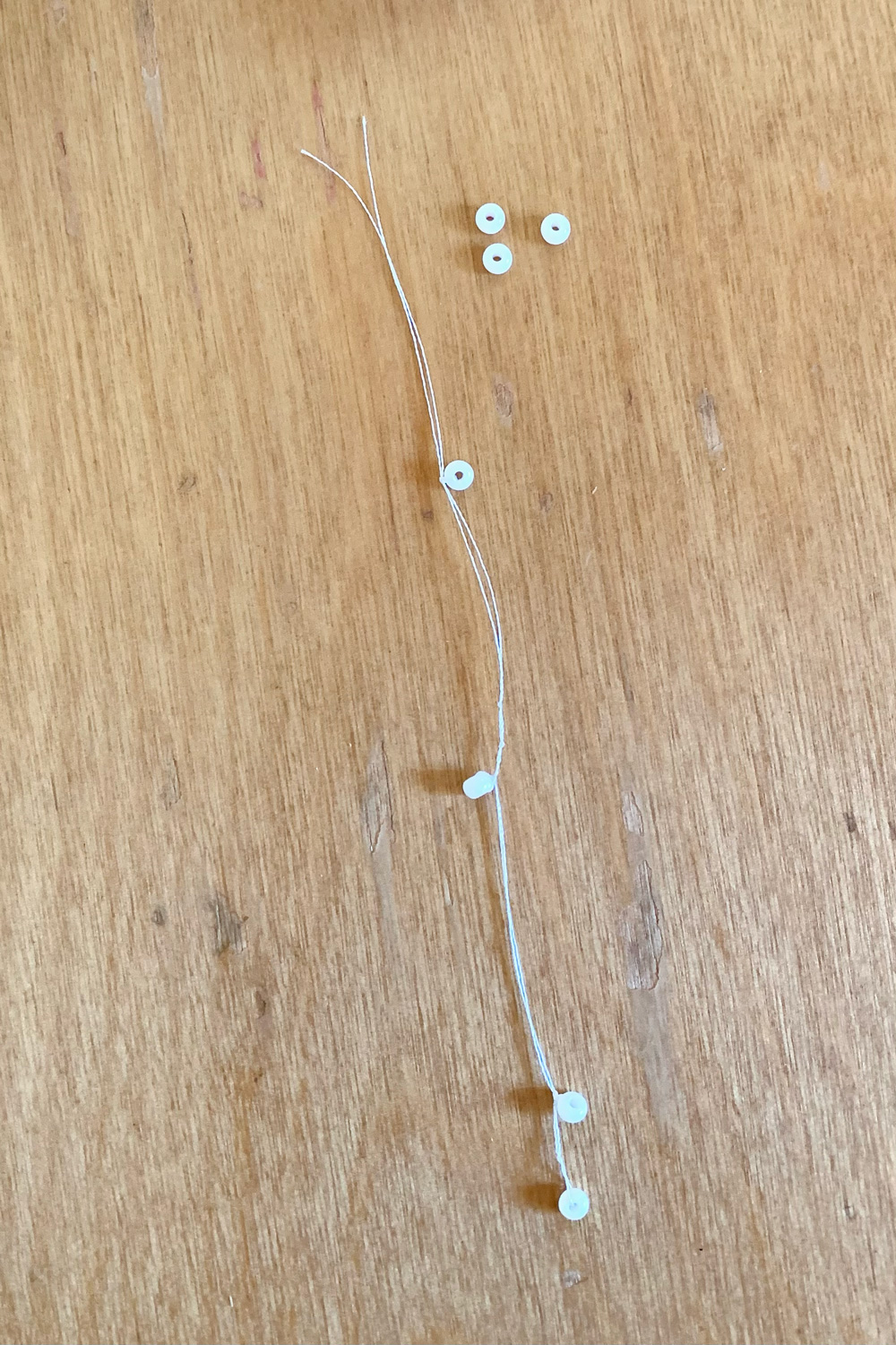A series of 4 white seed beads tied along the length of the white thread.