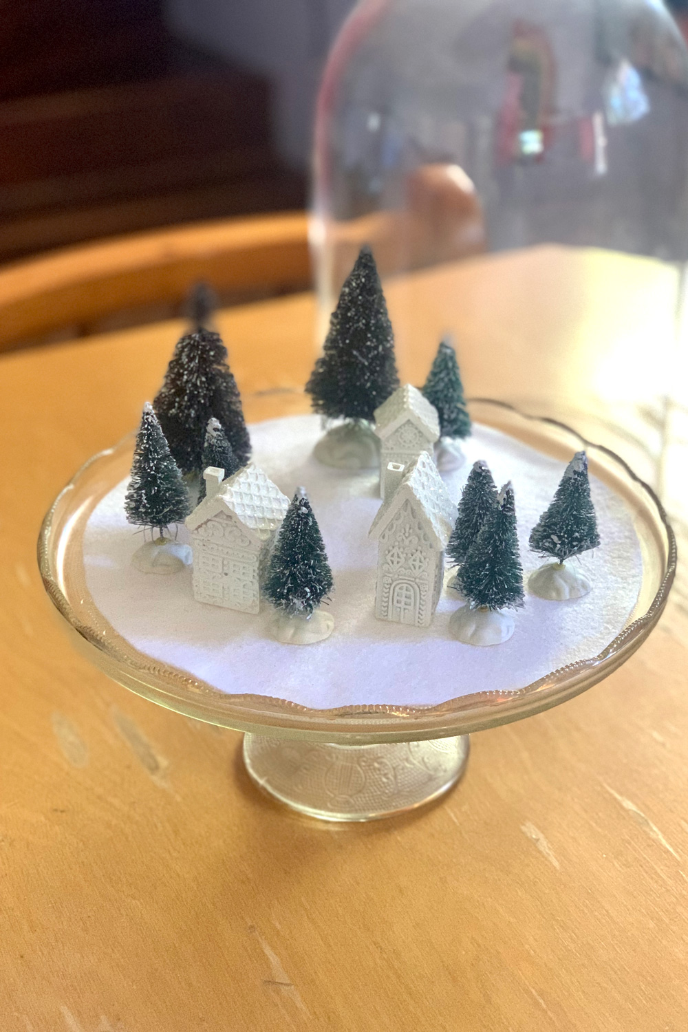 Several green trees and 3 white houses spread out over the white felt snowscape.