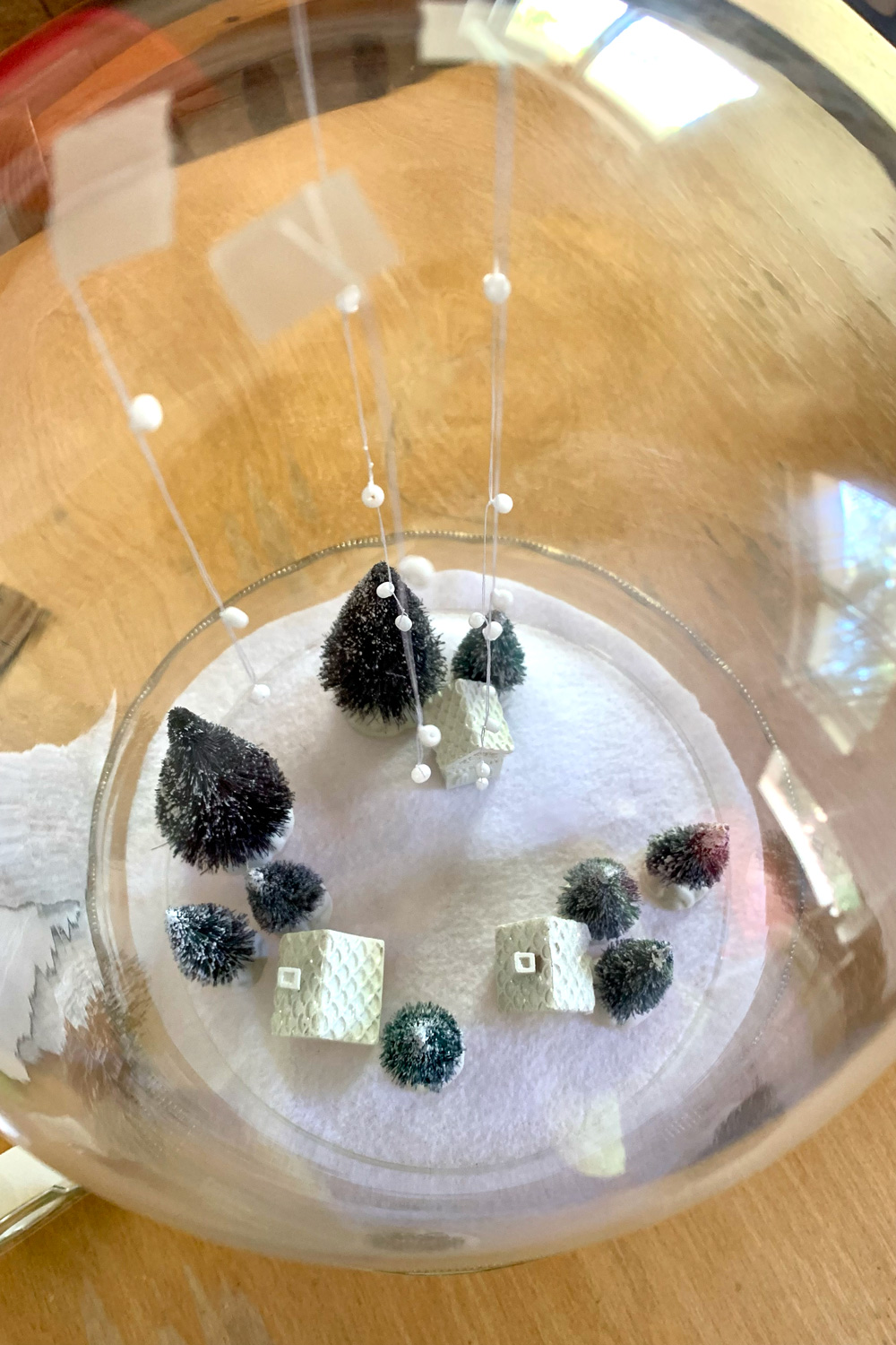 Bead and string snow taped to the top of a glass cloche dome.