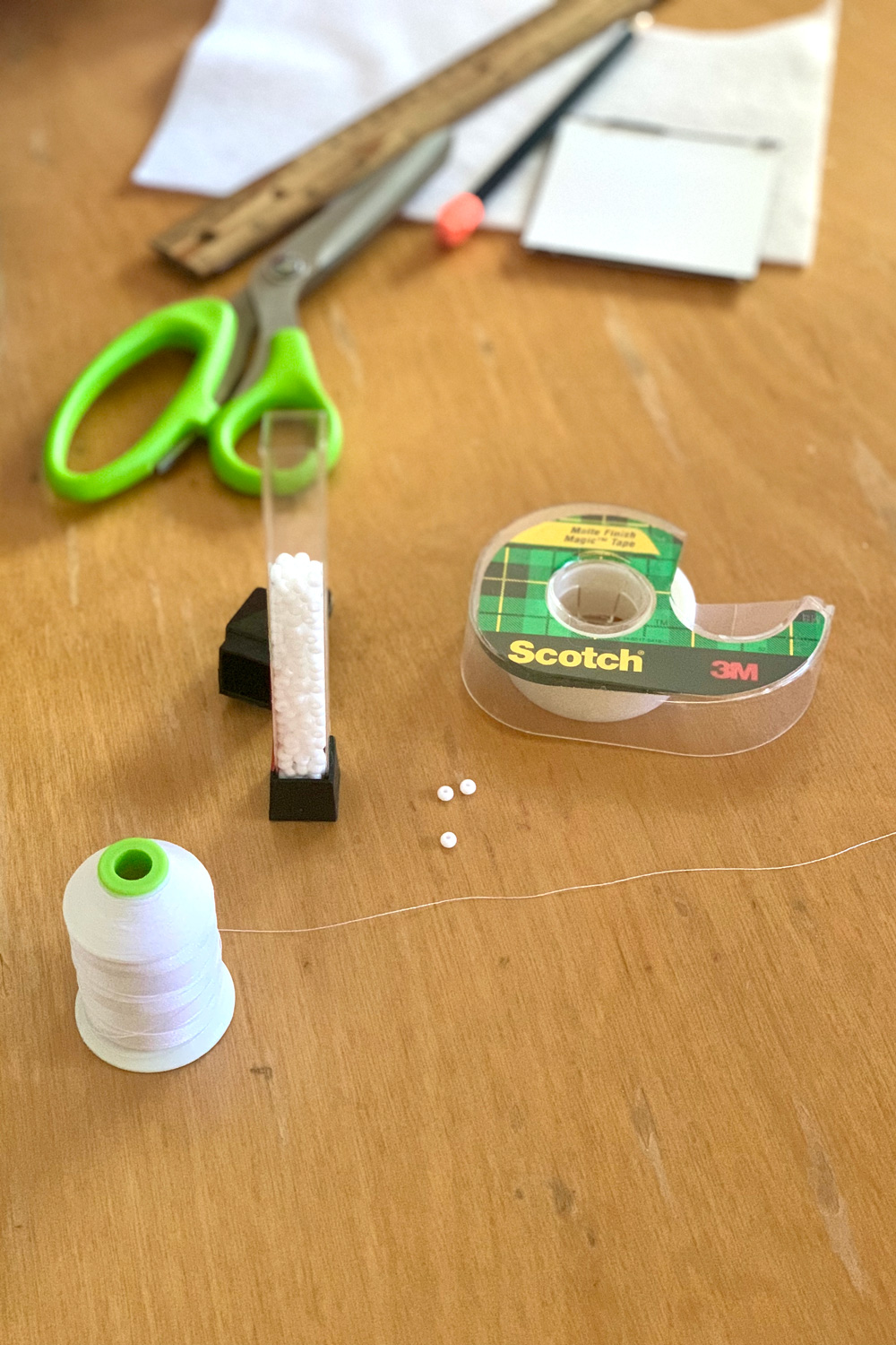 White thread beside a roll of tape and a jar of white seed beads.