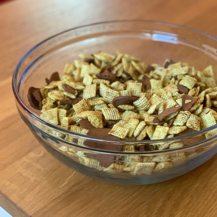 A glass bowl of buttery curry chex mix with cereal and rye chips.