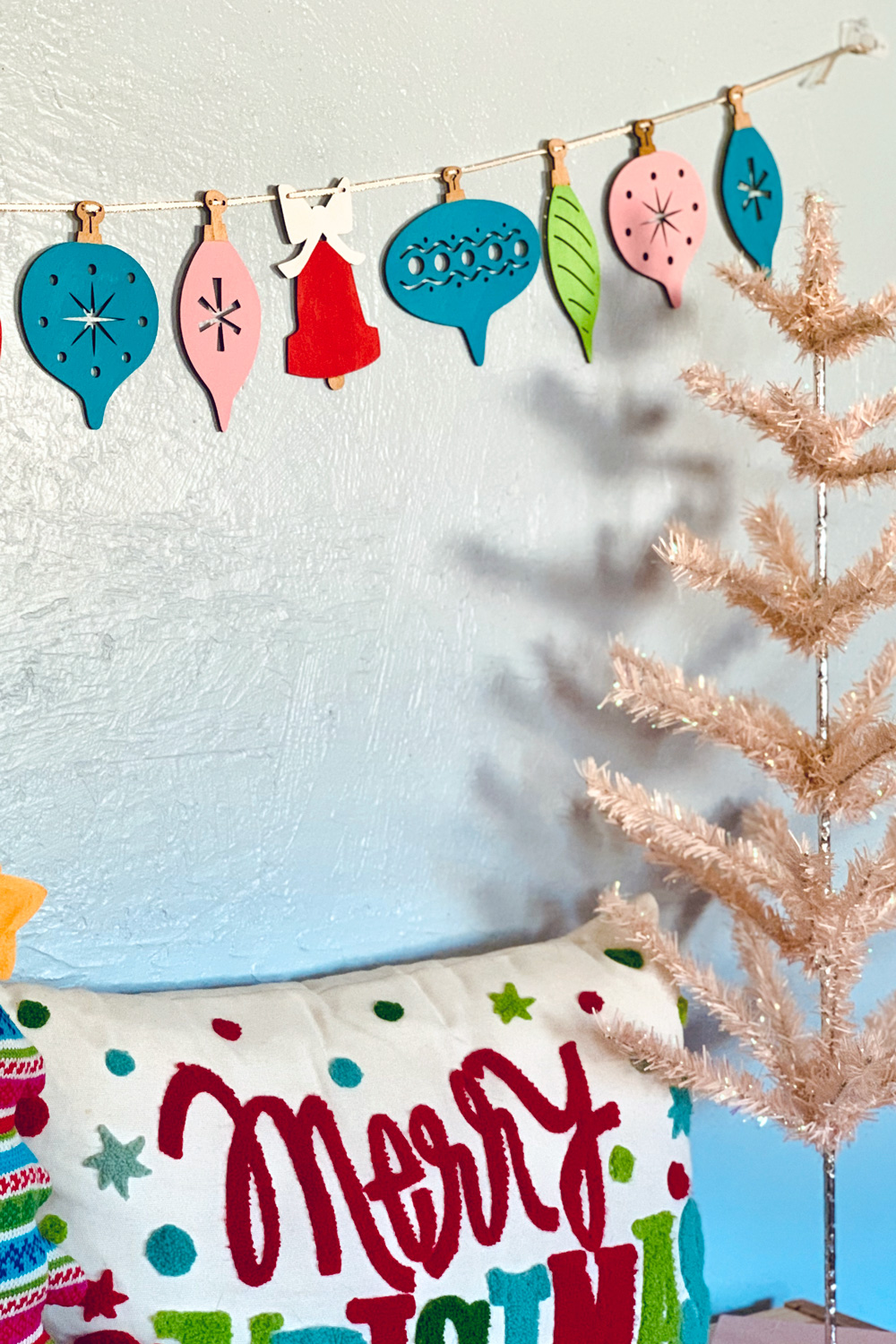 Colorful wood ornament garland beside a pink Christmas tree.