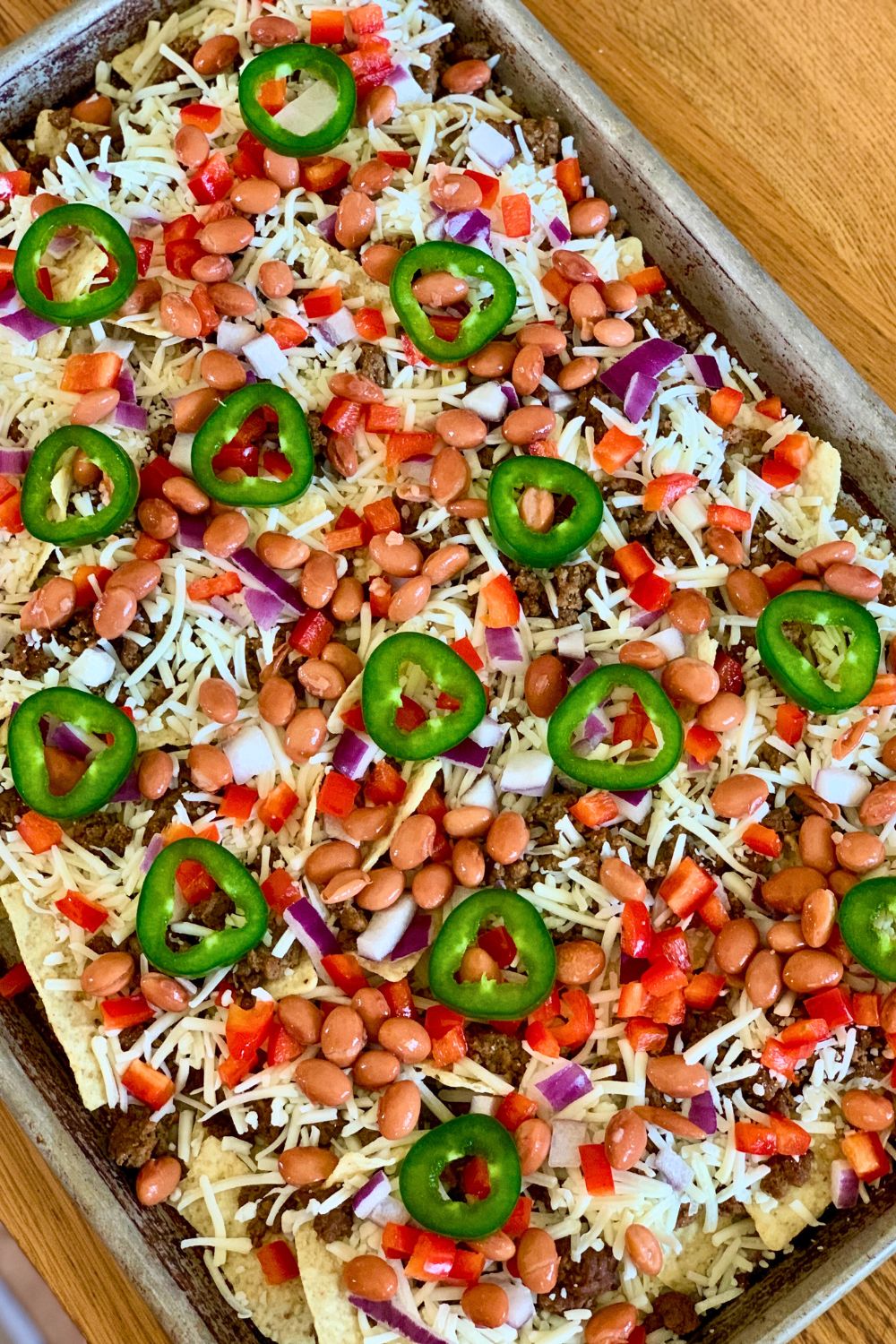 A sheet pan filled with chips, meat, beans, onion, cheese, and jalapeno slices.