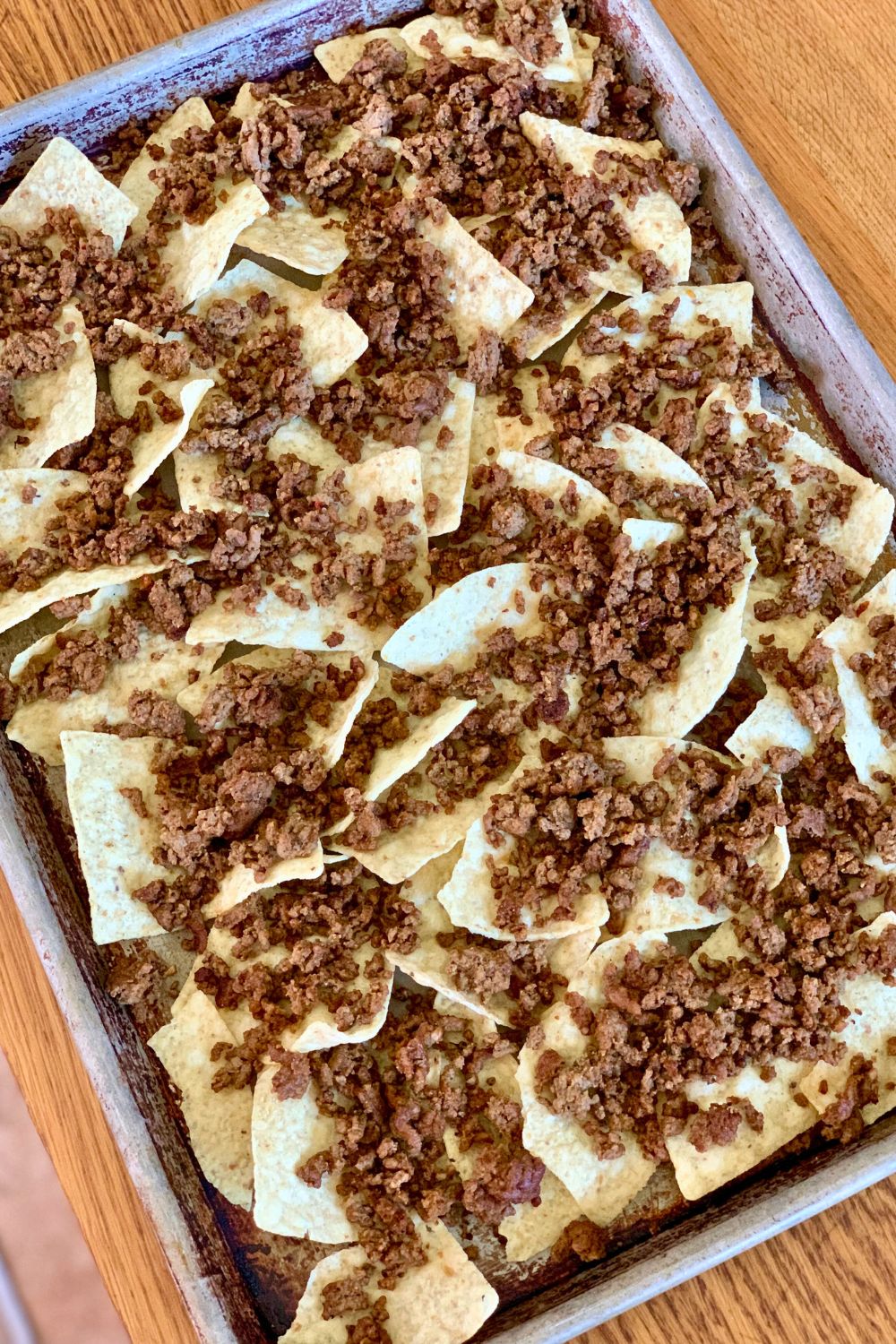 Cooked taco meat sprinkled over tortilla chips on a metal sheet pan.