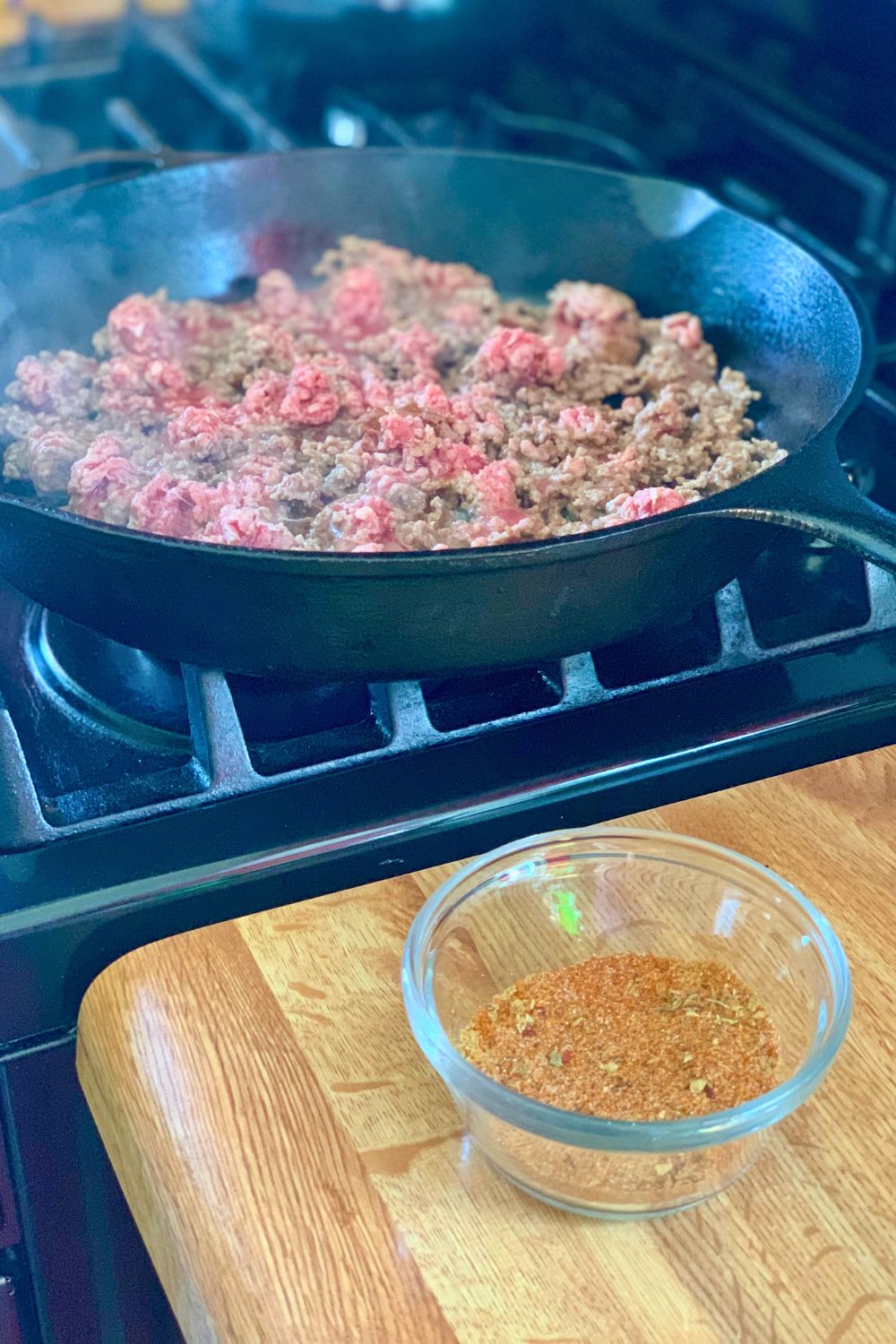 Ground beef in a cast iron skillet beside a small prep bowl of taco seasoning.
