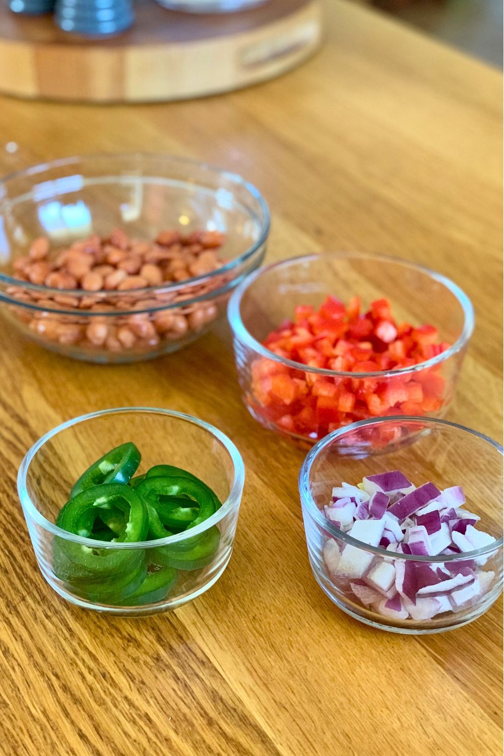 Glass bowls of pinto beans, diced red bell pepper, chopped red onions, and jalapeno slices.