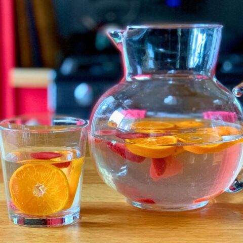 A pitcher of infused fruit water with sliced oranges and strawberries.