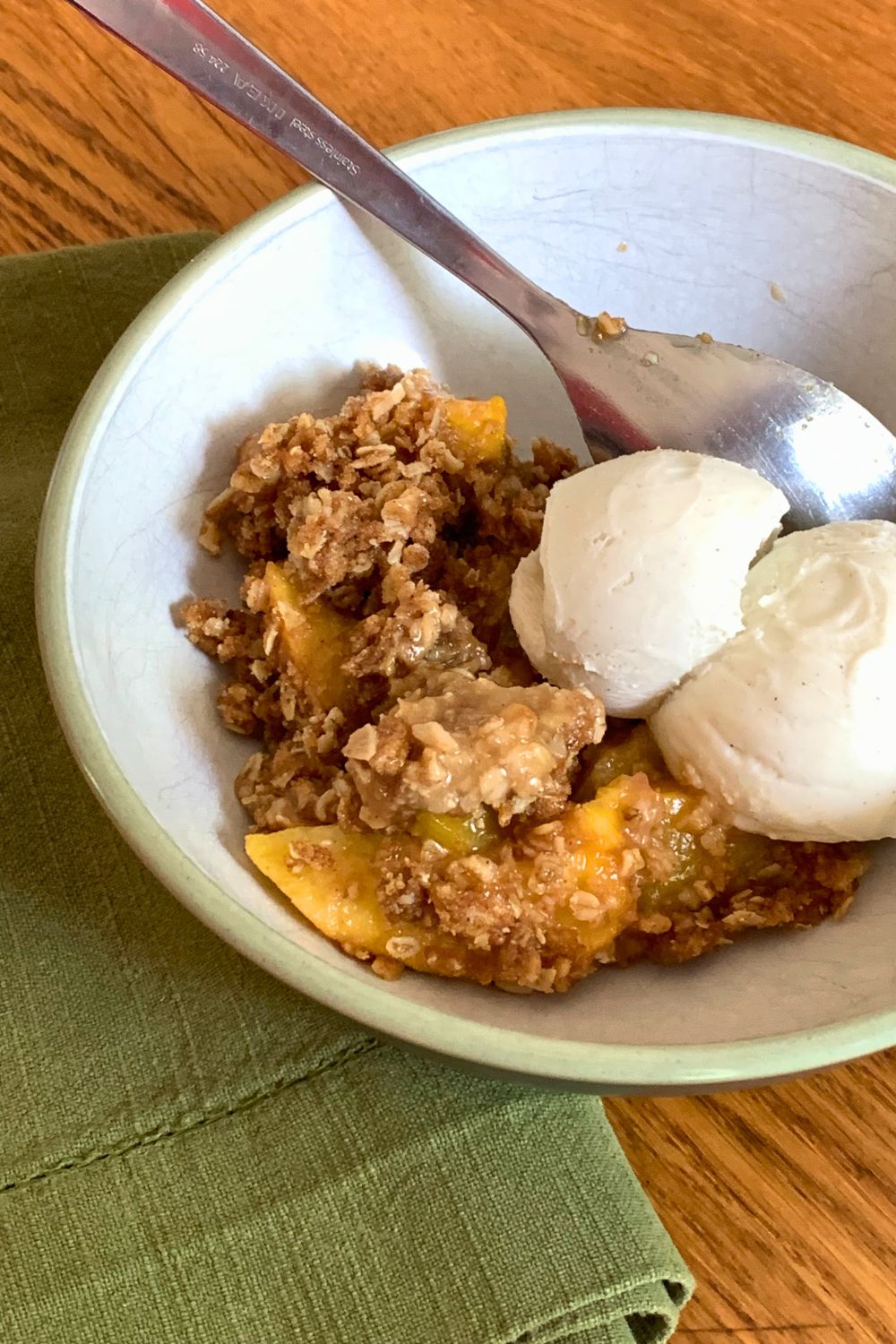A bowl of peach crisp served with a scoop of vanilla ice cream.