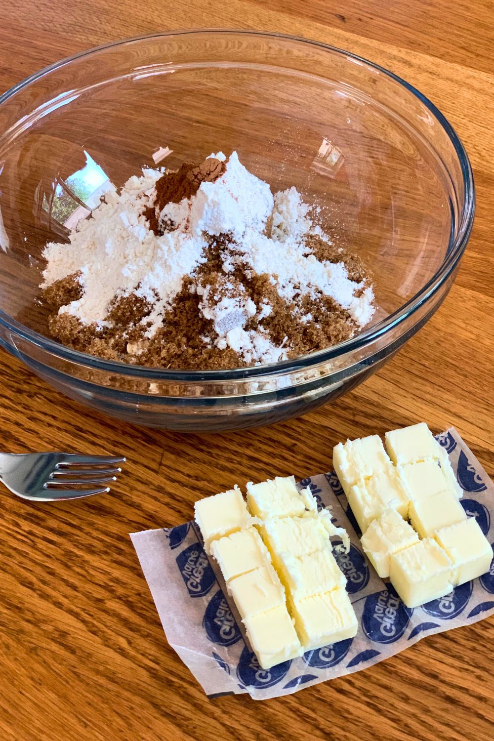 Dry ingredients in a glass bowl beside butter cubes.