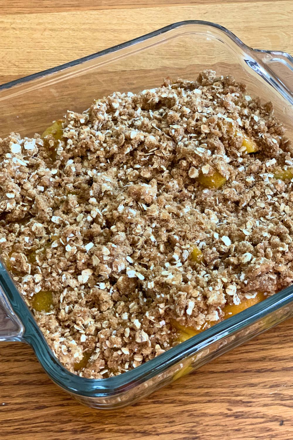 Unbaked peaches with crumb topping in a glass dish.