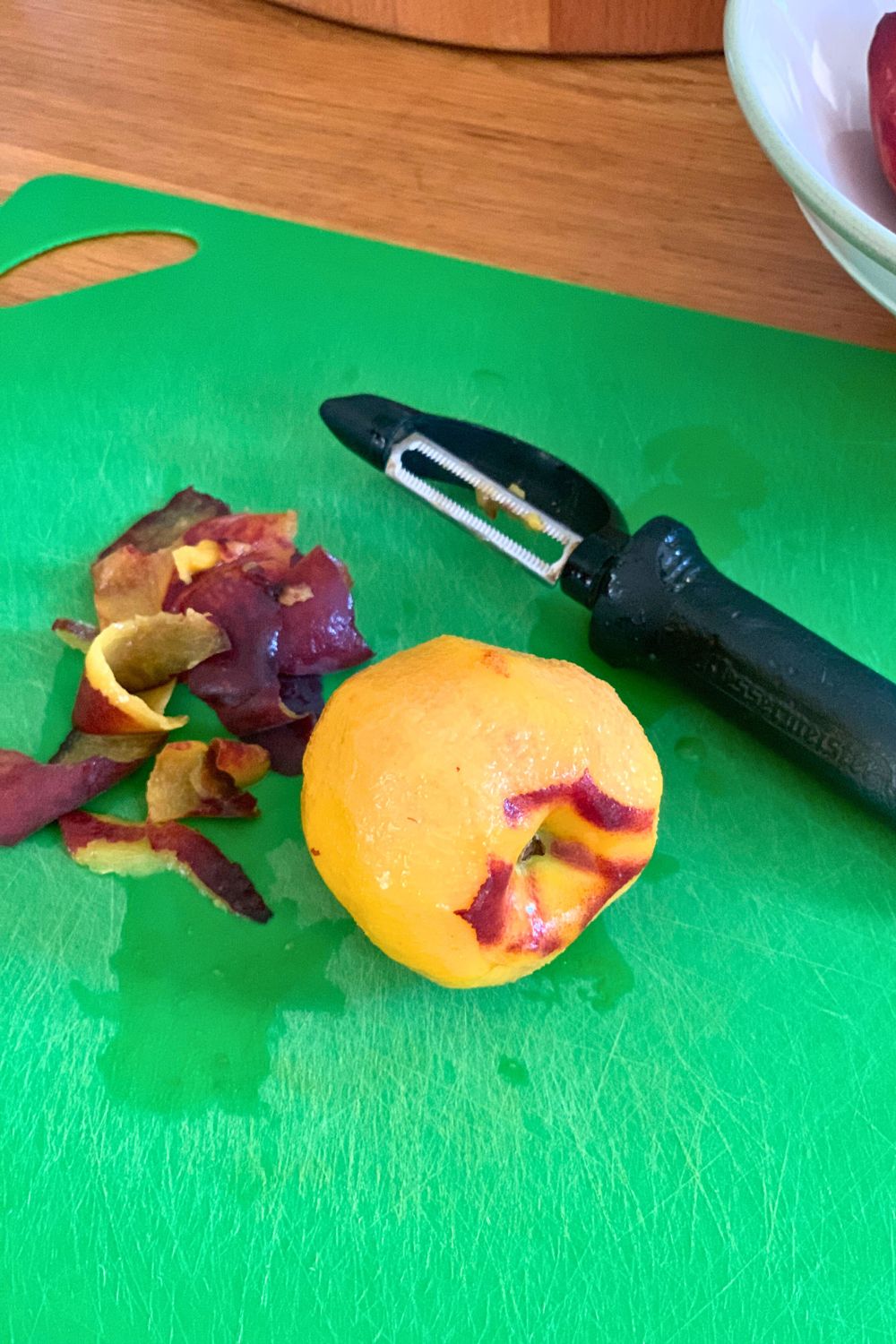 A vegetable peeler beside a freestone peach with the peel removed.