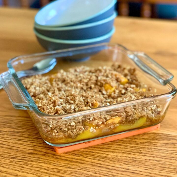 A glass casserole dish of homemade baked peach fruit crisp.