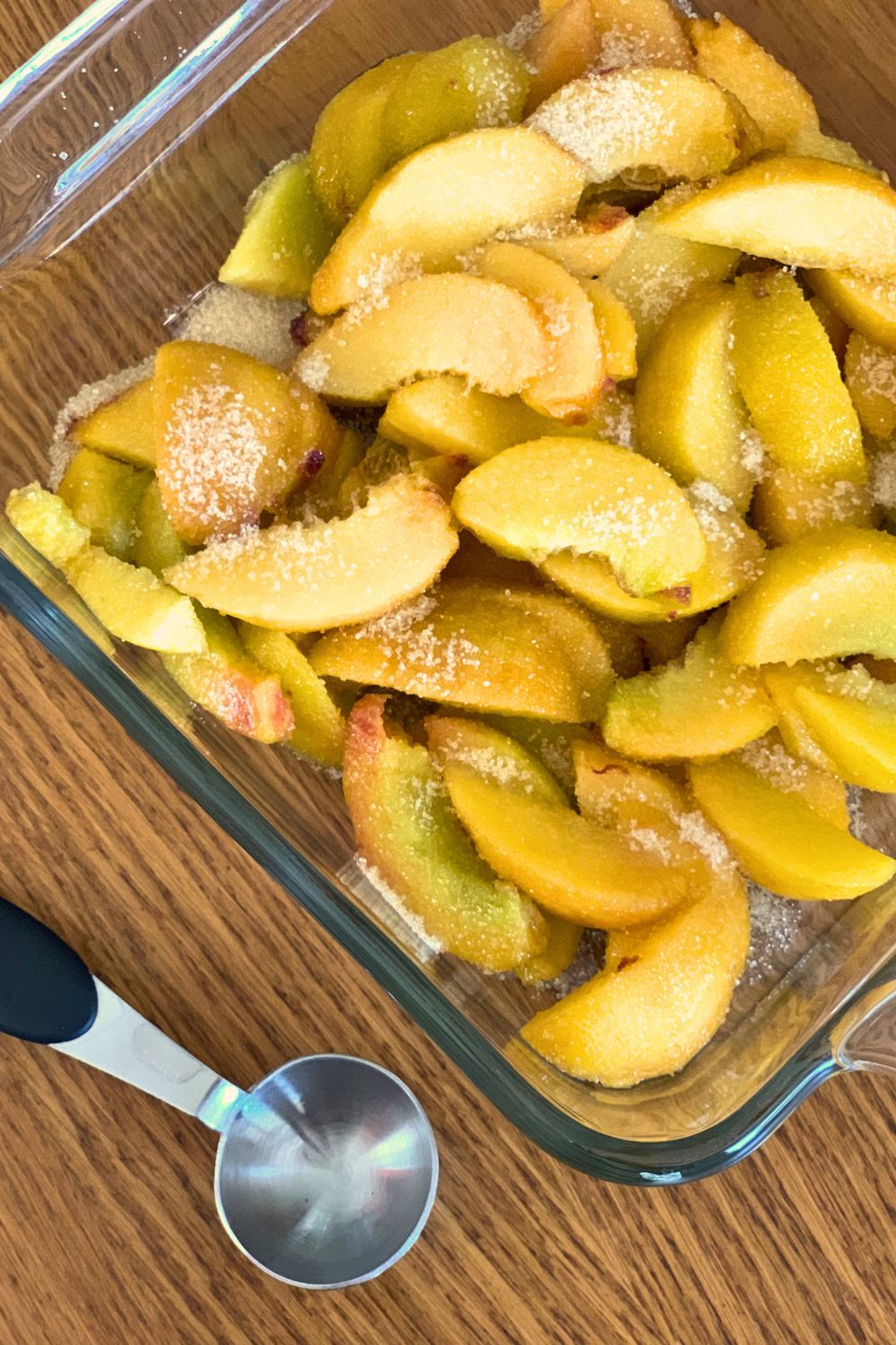 A glass baking dish filled with sliced peaches sprinkled with sugar.