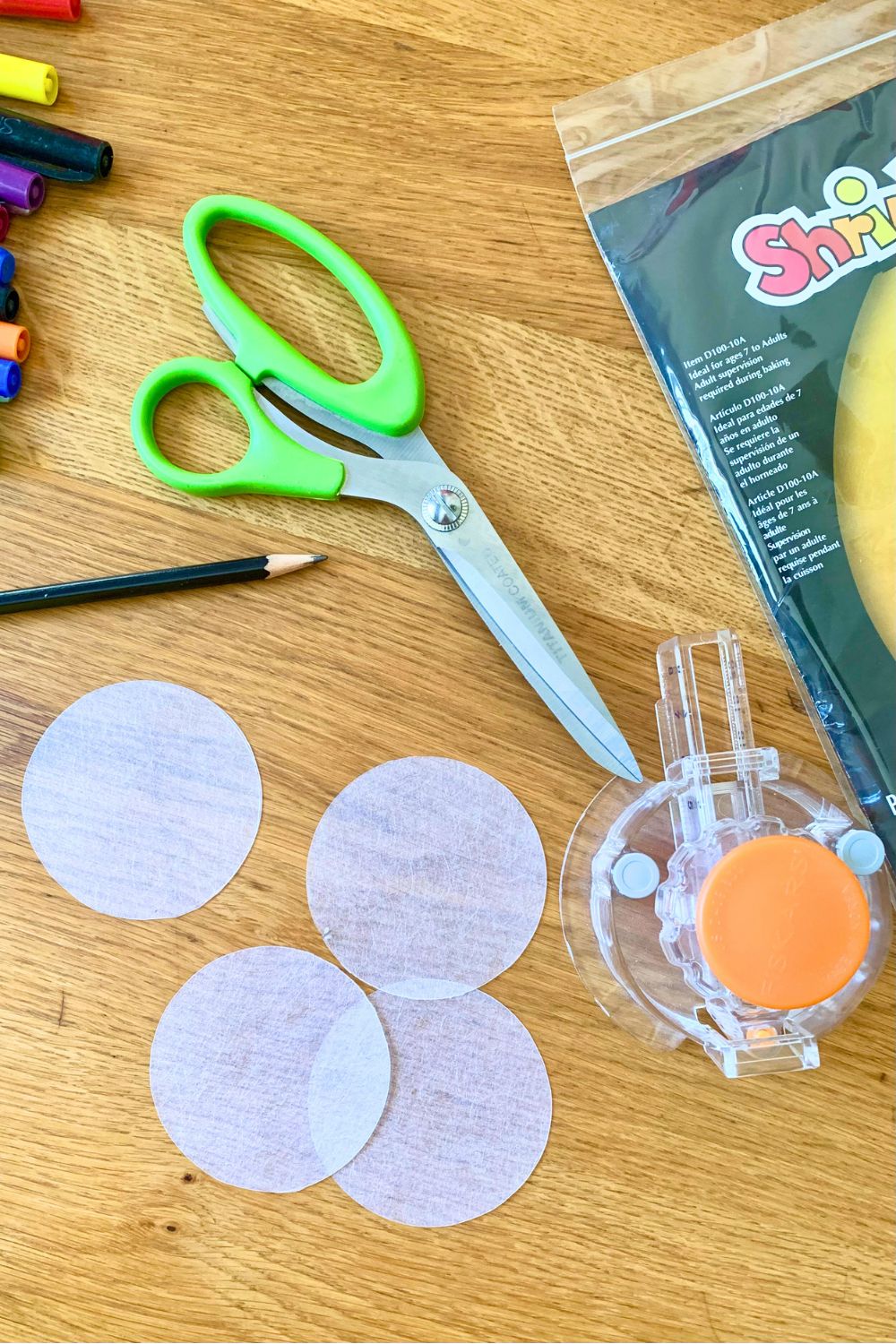 Scissors and a circle punch beside 4 shrink plastic circles.