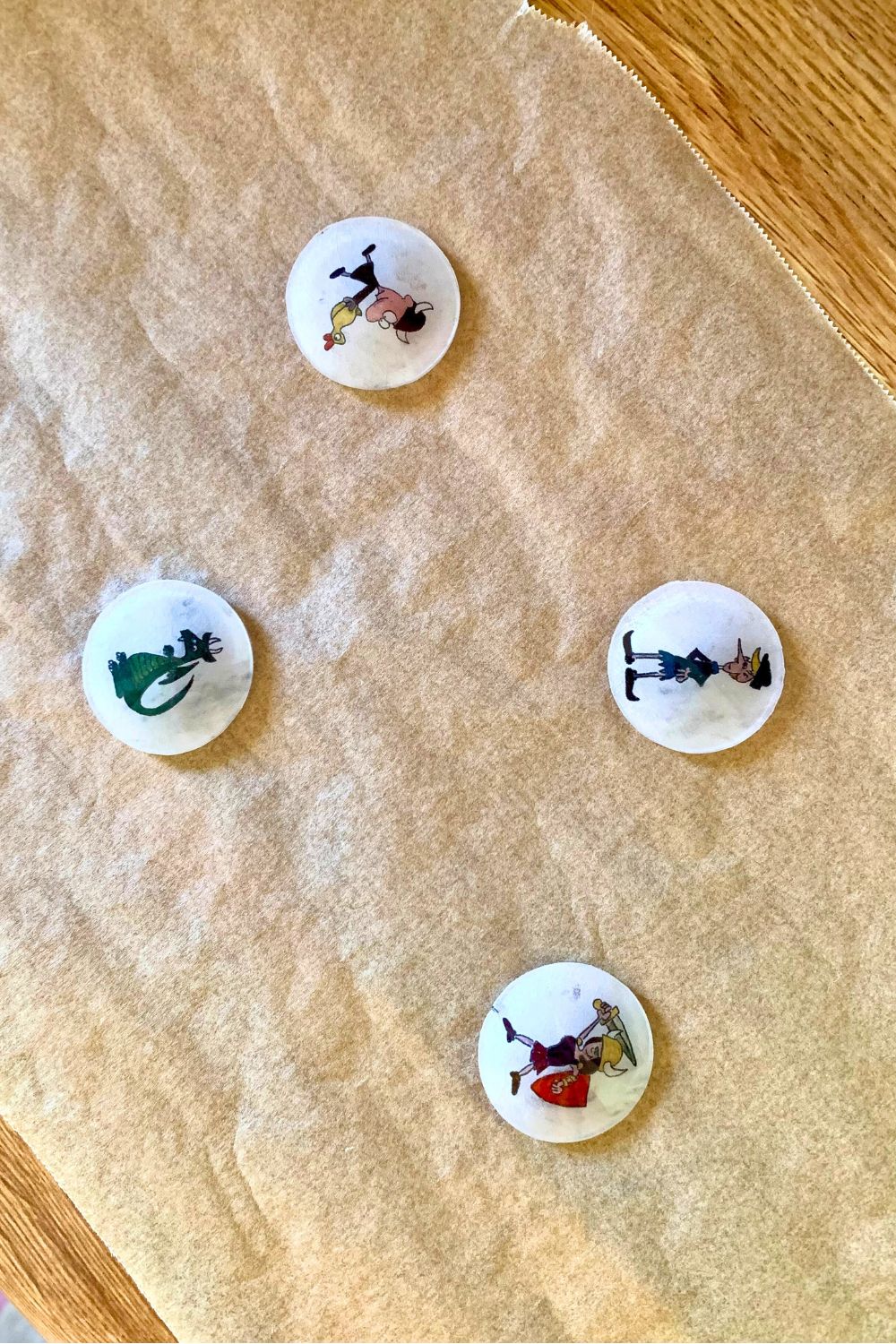 A set of 4 decorated Shrinky Dink circles cooling on parchment paper.