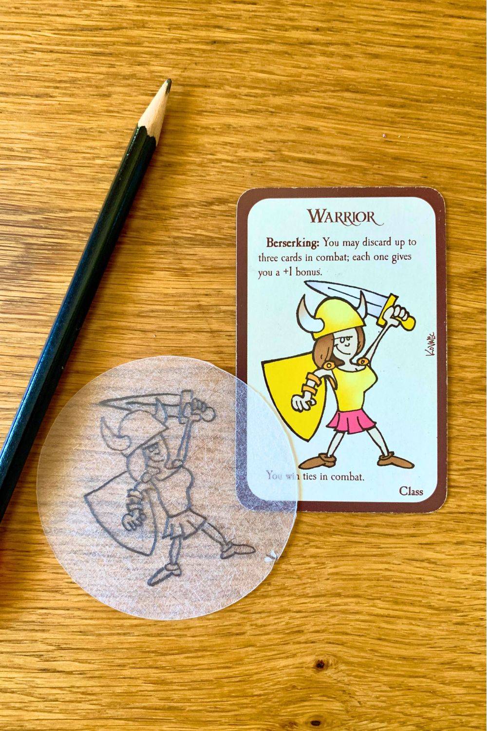 A Munchkin game card with a warrior girl beside a circle of Shrinky Dink plastic with a tracing.