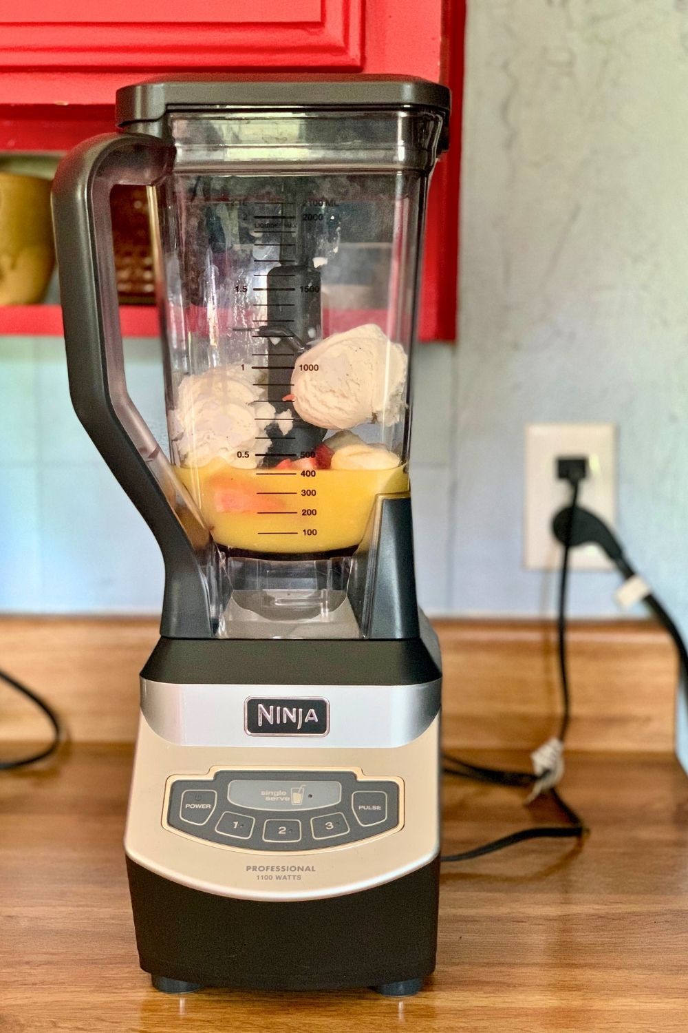 Blender pitcher filled with strawberries, banana, ice cream, and orange juice.