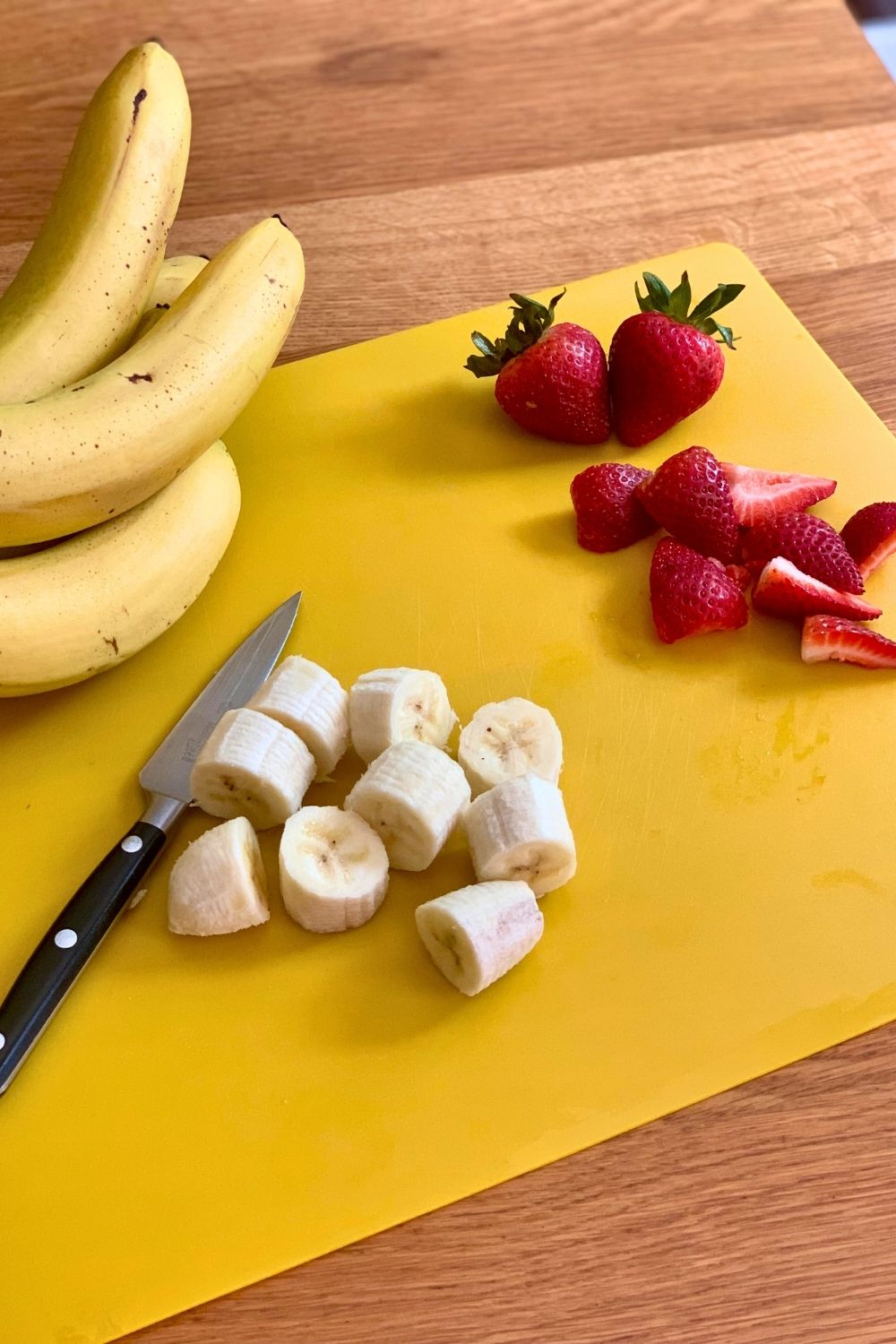 Sliced strawberries and banana on a yellow cutting board.