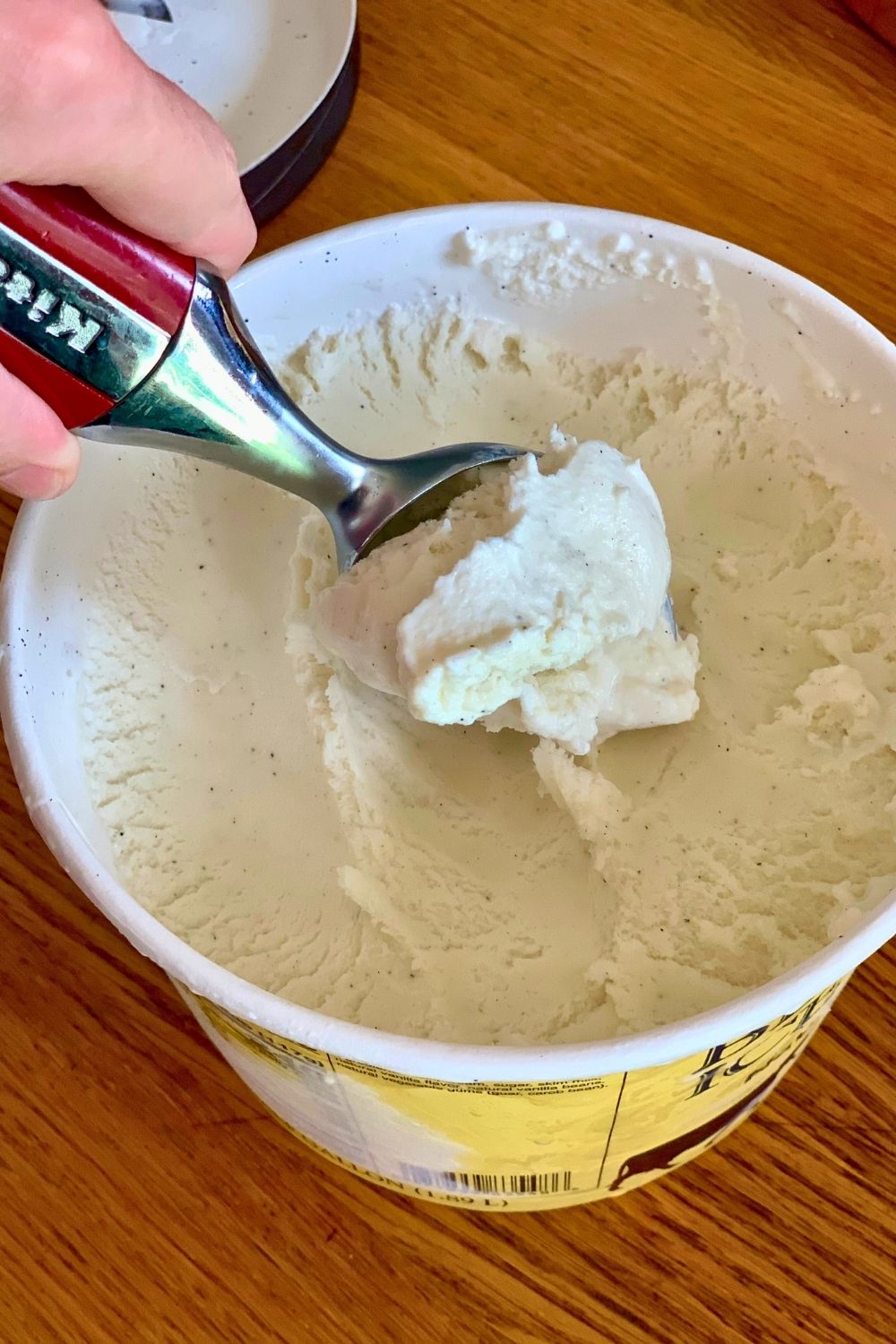 Hand scooping vanilla ice cream from a carton.