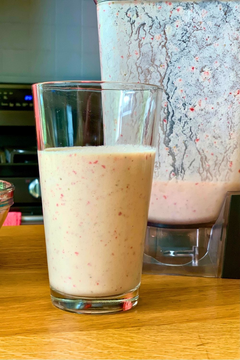 Orange sunrise smoothie in a glass beside a blender pitcher.
