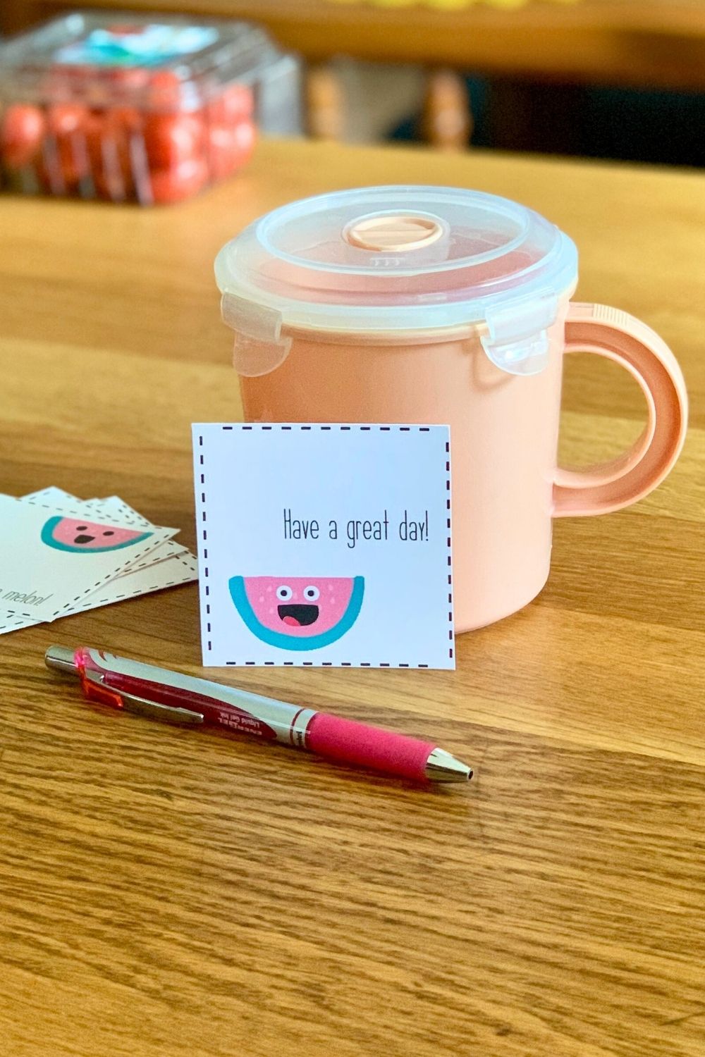 A square notecard that reads 'Have a great day' with a smiling watermelon leaning against a snack cup.