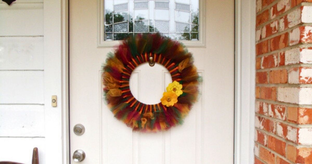 A fall tulle wreath in maroon, forest green, and marigold with felt flowers hanging on a door.