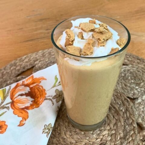 A pumpkin smoothie in a glass topped with whipped cream and graham cracker pieces.