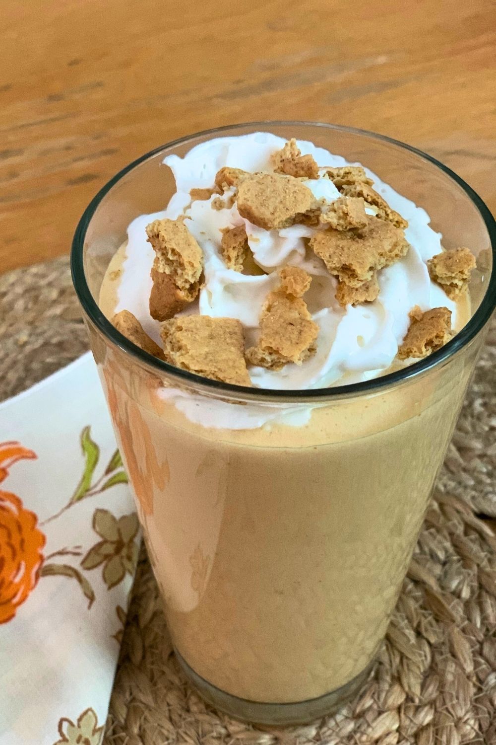 A glass filled with a golden orange pumpkin smoothie topped with whipped cream and graham crackers.