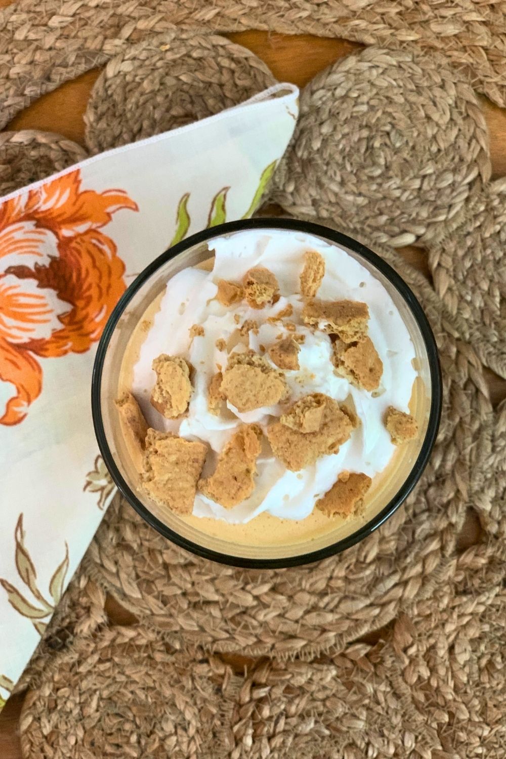 Overhead view of graham cracker pieces and whipped cream on top of a filled glass.