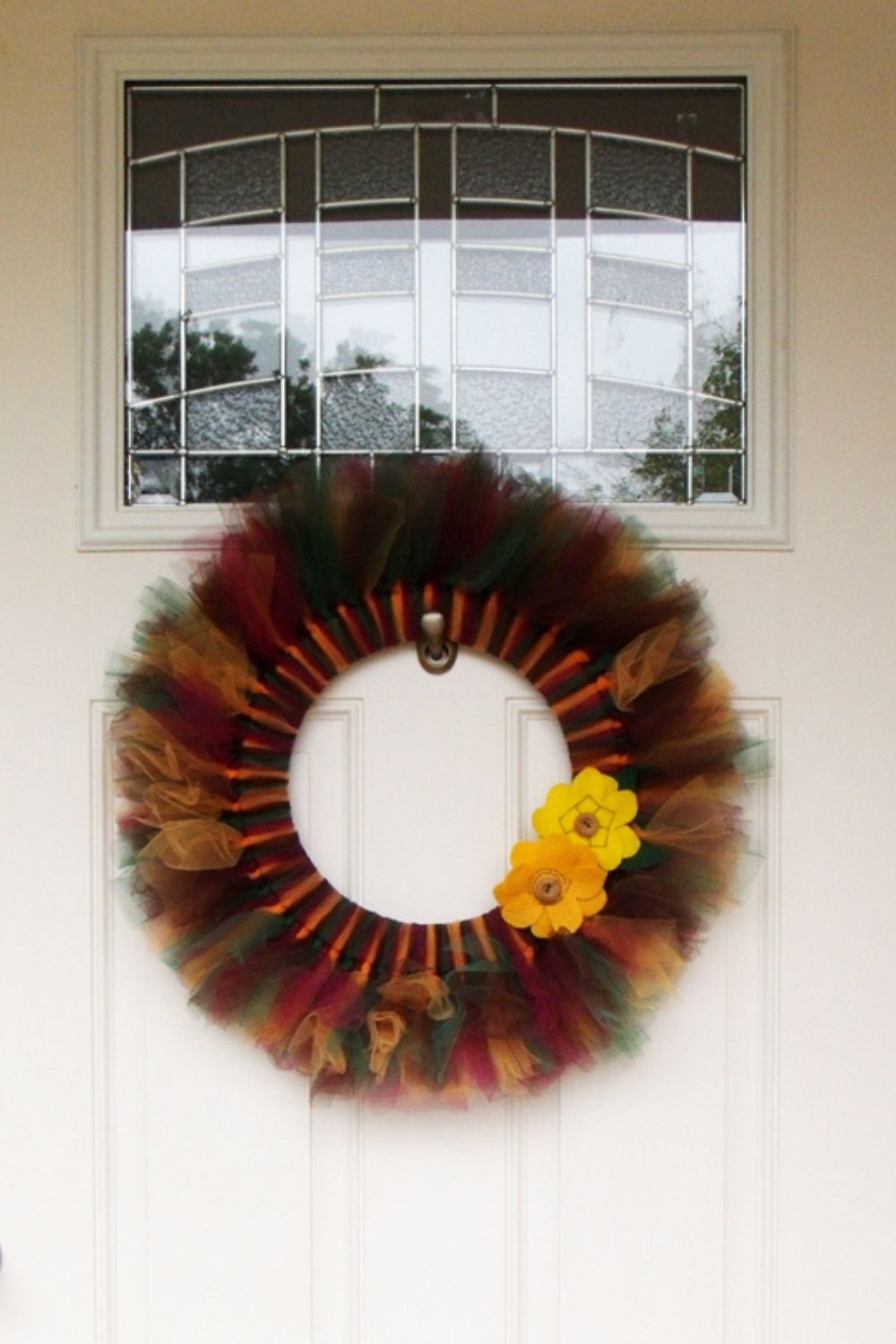 A fall tulle wreath in maroon, forest green, and marigold with felt flowers hanging on a door.